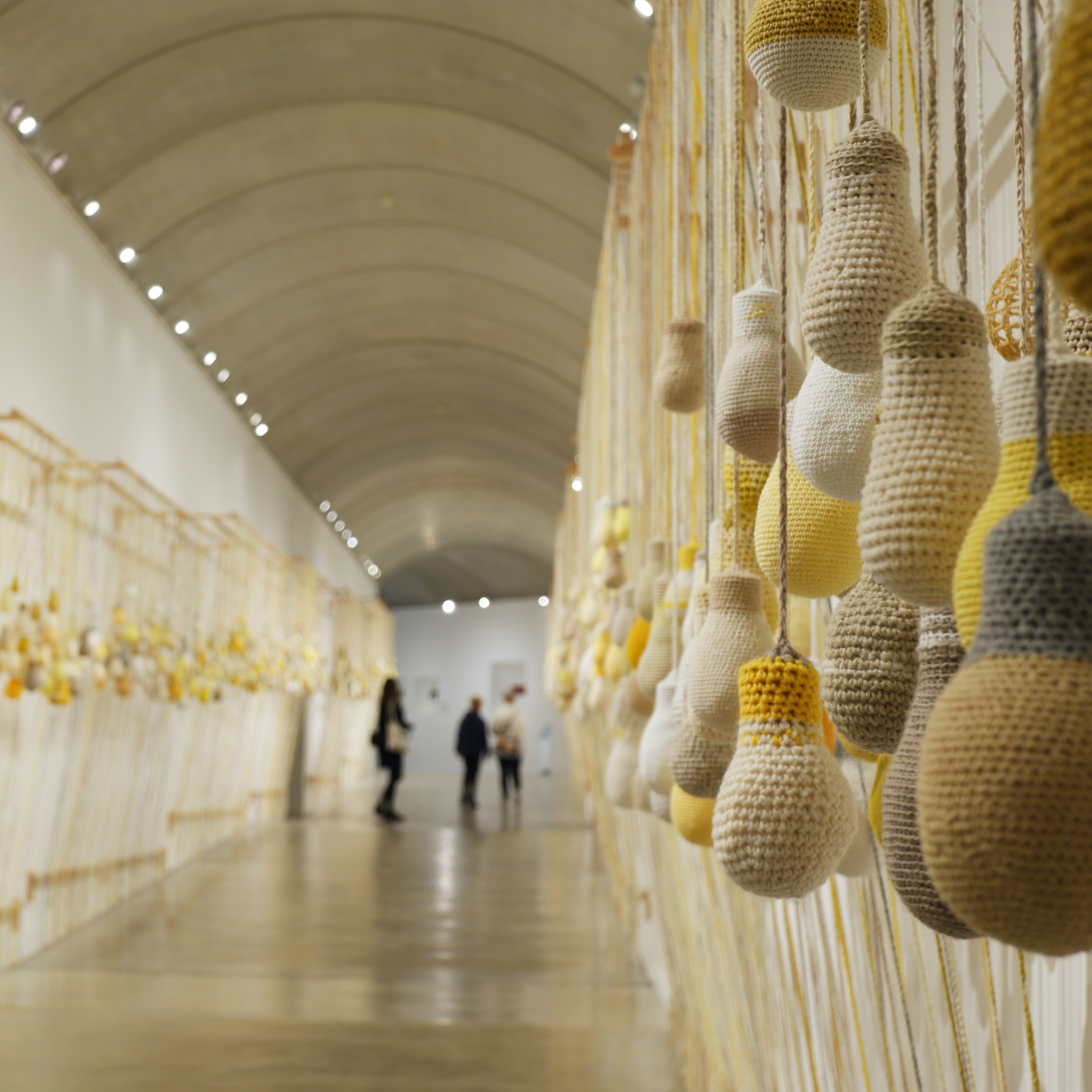 hundreds of crocheted light bulbs hanging along the walls of a gallery